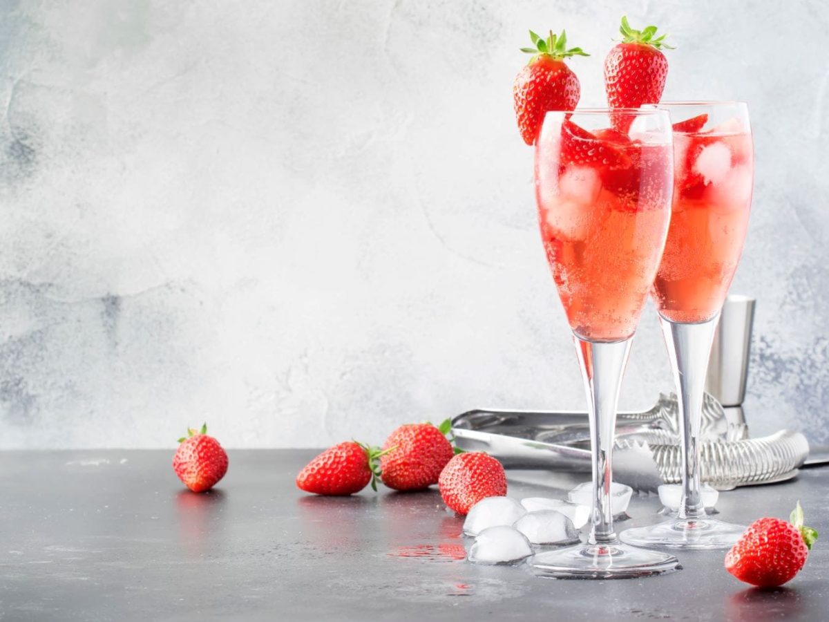 Aperitif Sektempfang zwei Rossini limone auf hellgrauem Untergrund und Hintergrnd mit Erdbeeren. Im Bild weitere Erdbeeren. Frontalansicht.