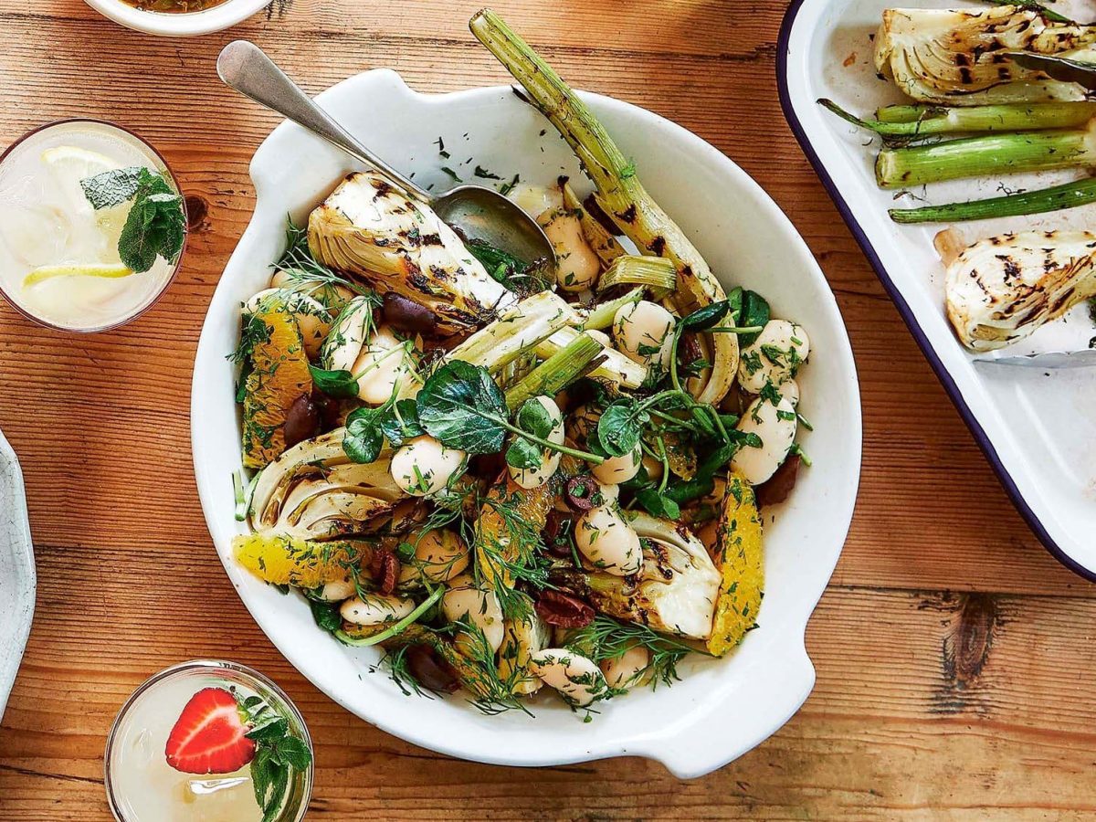 Salat mit gegrilltem Fenchel, Orange und Dill in einer Schüssel in der Draufsicht, daneben eine Auflaufform mit gerilltem Fenchel und Getränkegläser.