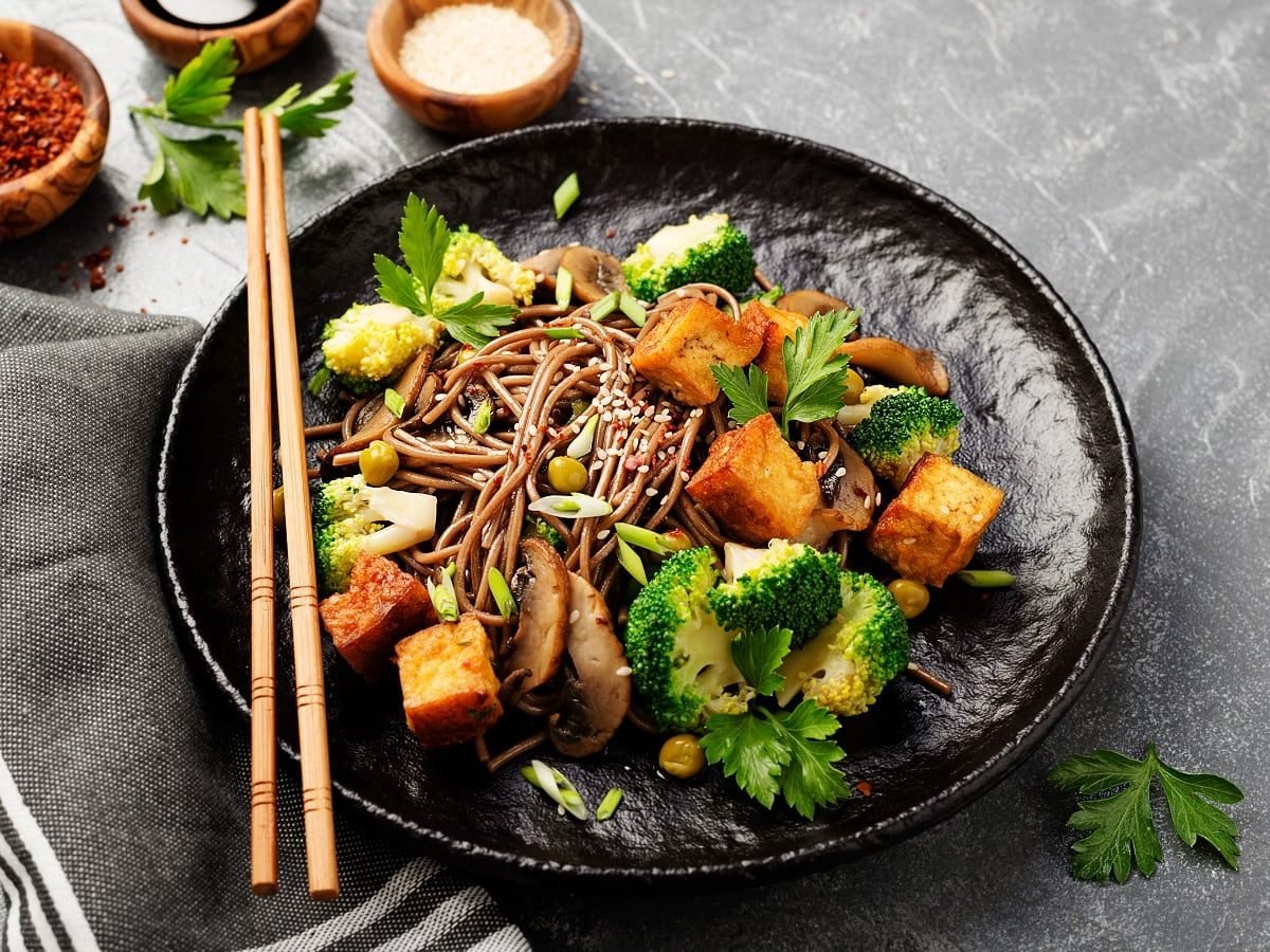 Ein schwarzer Teller mit Soba-Nudelsalat auf einem grauen Steinuntergrund.