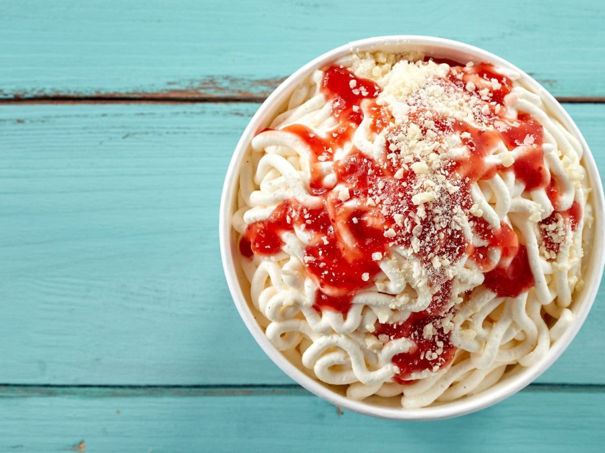 Ein Becher Spaghetti-Eis mit Erdbeersauce und Schokosplittern in der Draufsicht.