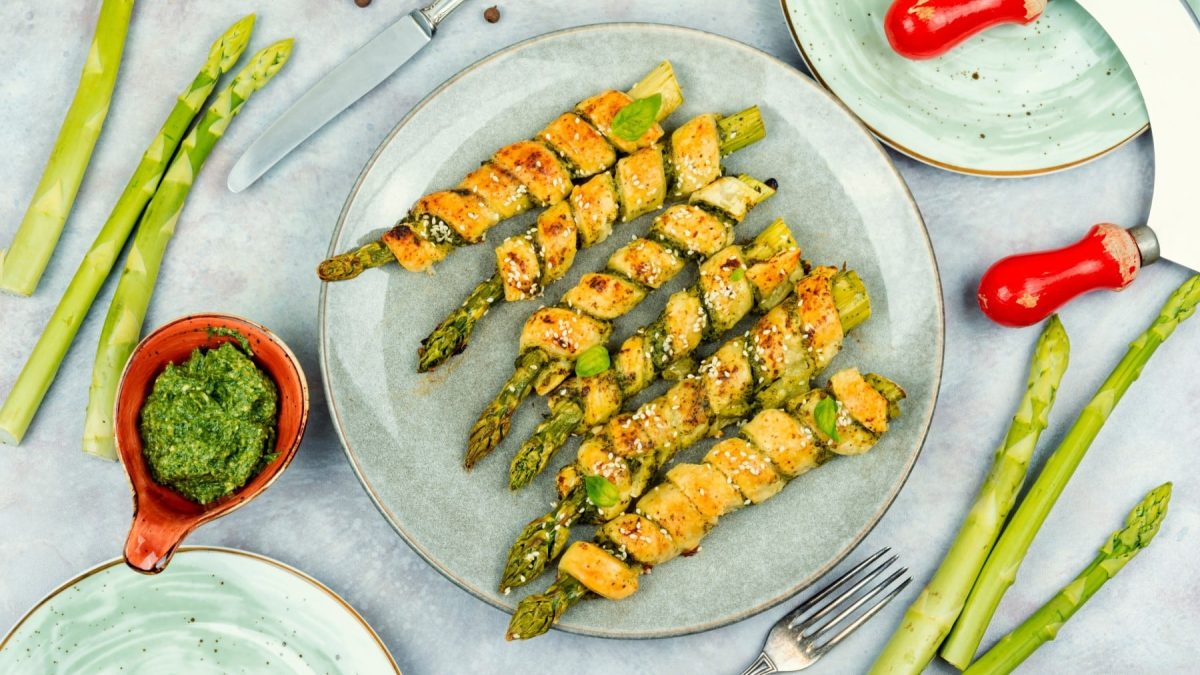 Draufsicht: Teller mit Spargel im Grissini-Mantel, drum herum Gabel, Messer, weitere Teller, Schale Pesto und grüne Spargelstangen.