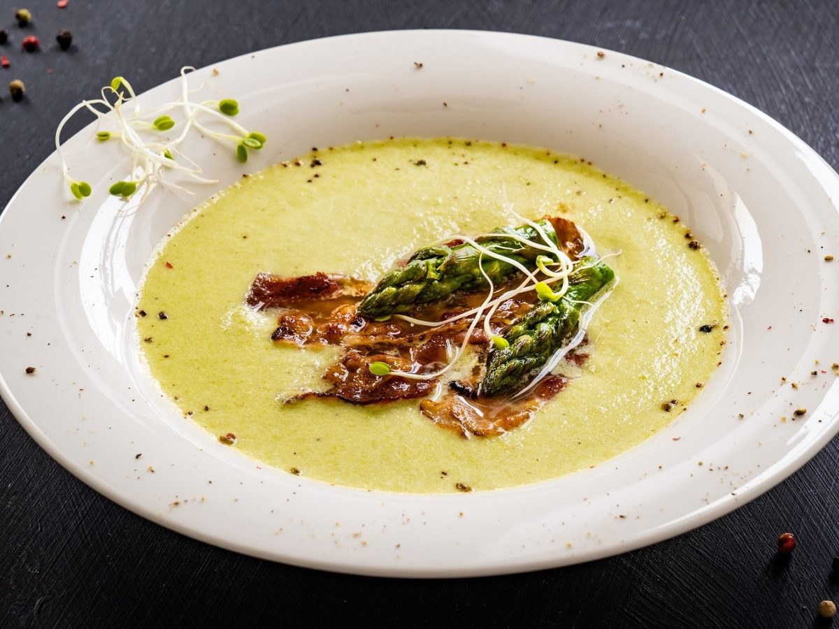 Ein weißer Teller mit der Spargel-Kartoffelcremesuppe auf dunklem Untergrund.