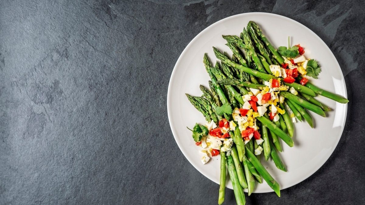 Grüner Spargel polnischer Art mit gehackten Eiern und Tomaten auf weißem Teller