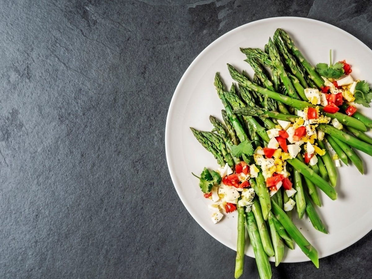 Grüner Spargel polnischer Art mit gehackten Eiern und Tomaten auf weißem Teller