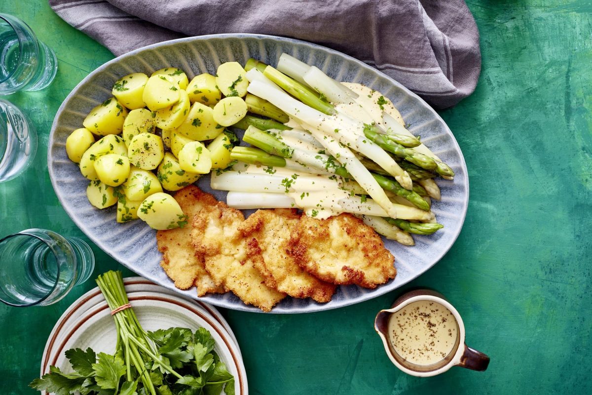 Auf einem Teller ist eine Spargelplatte mit Hähnchenschnitzel angerichtet. Sie ist mit Petersilie bestreut.