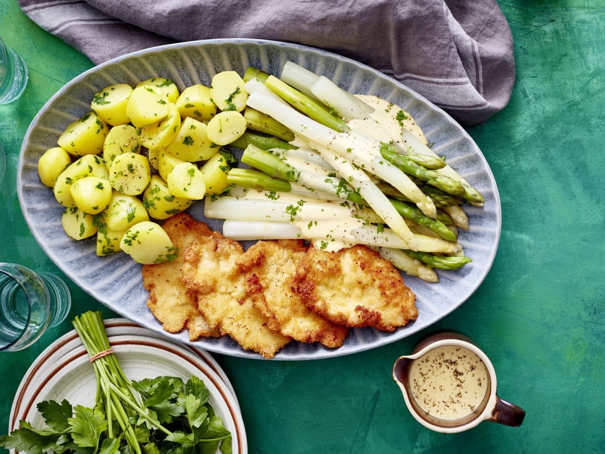 Auf einem Teller ist eine Spargelplatte mit Hähnchenschnitzel angerichtet. Sie ist mit Petersilie bestreut.