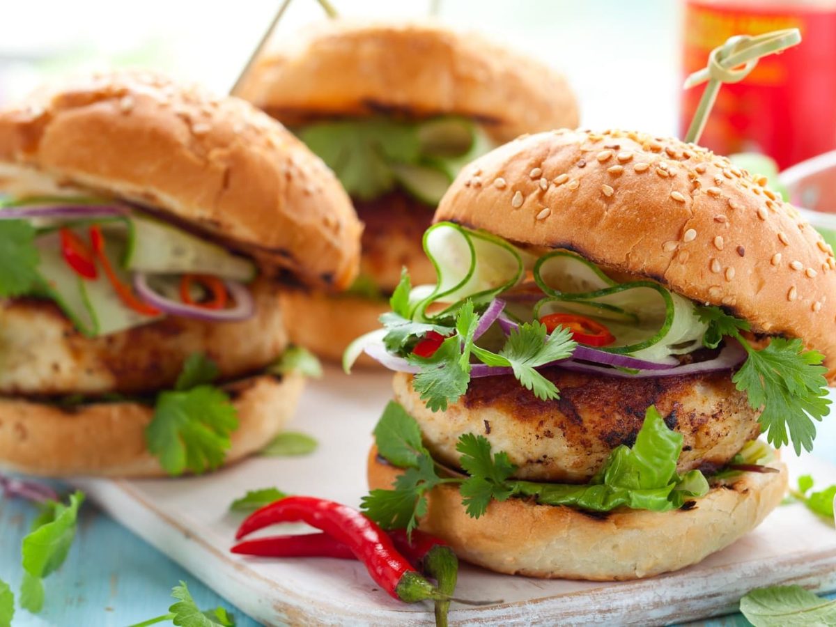 Drei Thai-Chicken-Burger auf einem hellblauen Holztisch.