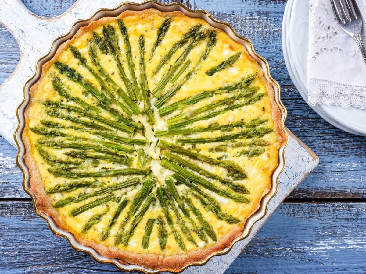 Eine vegane Spargel-Quiche in der Draufsicht, daneben Teller und Besteck.