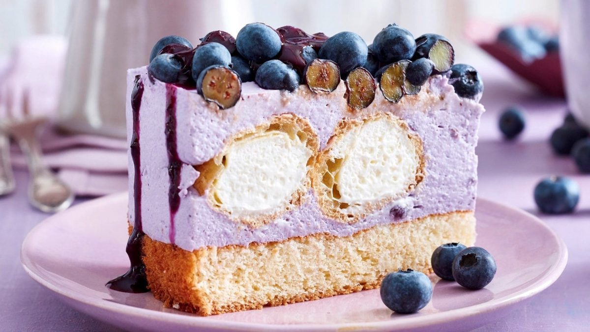 Auf einem Teller steht eine Windbeutel-Joghurt-Torte. Sie ist mit Heidelbeeren belegt.