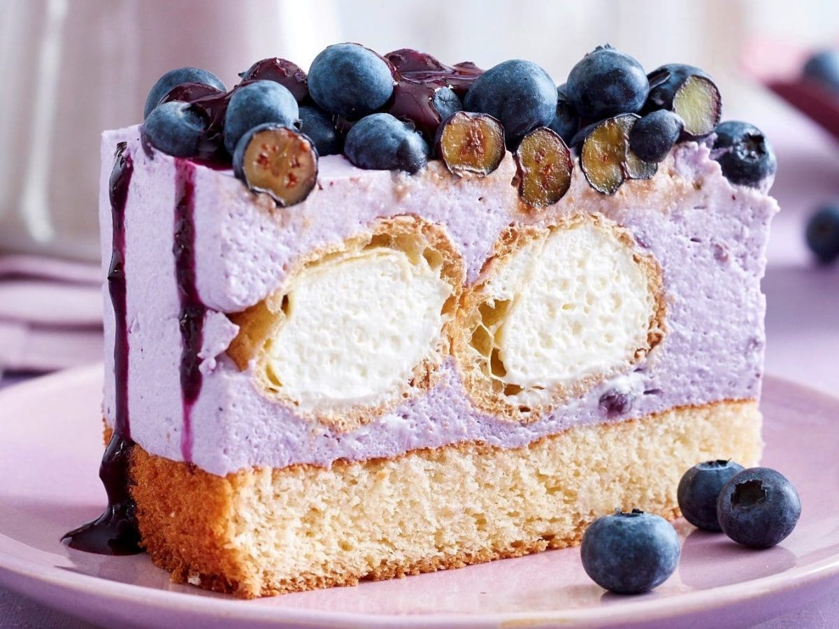 Auf einem Teller steht eine Windbeutel-Joghurt-Torte. Sie ist mit Heidelbeeren belegt.