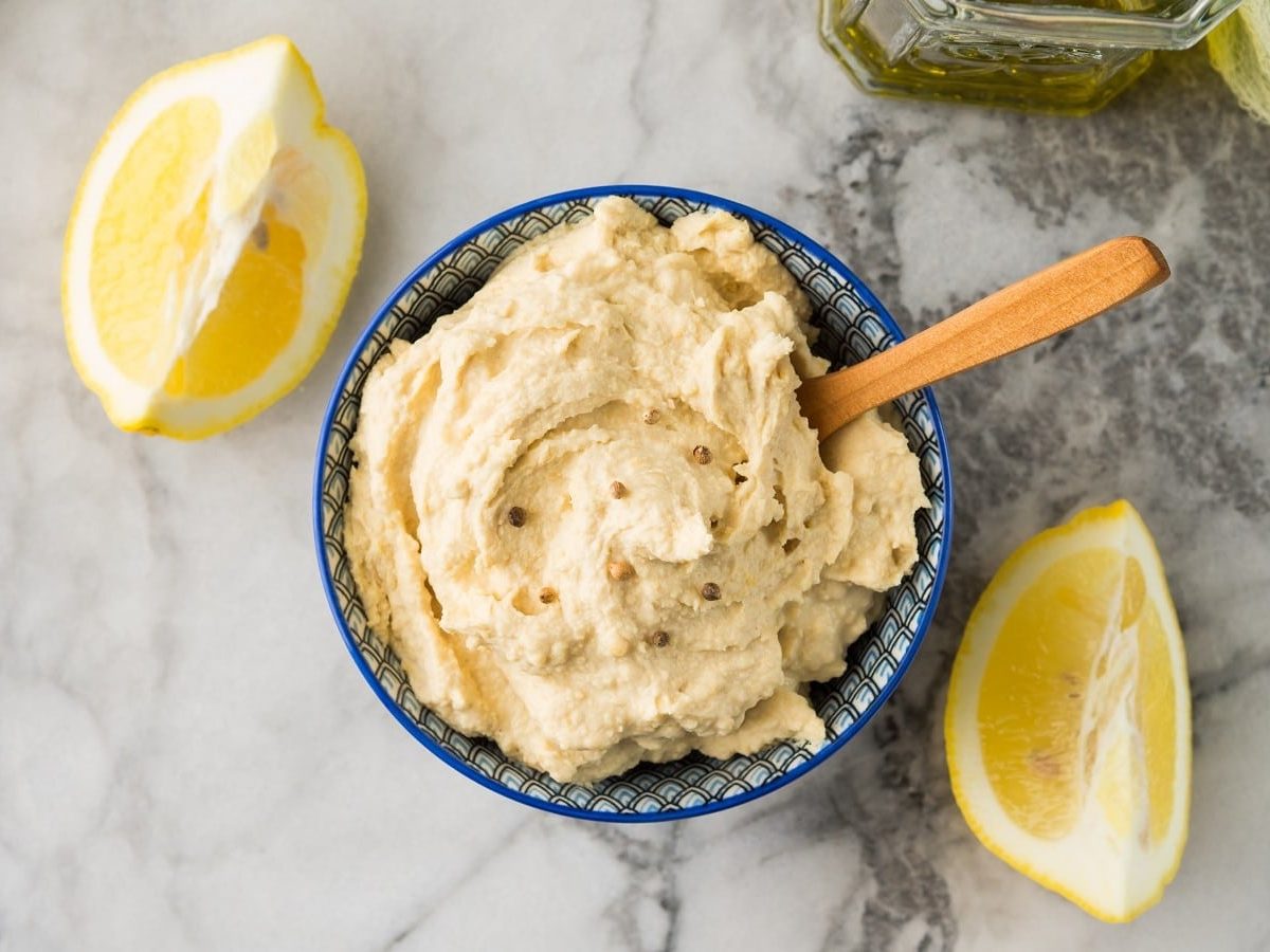 Eine blaue Schüssel mit Zitronen-Hummus auf einem Marmortisch.