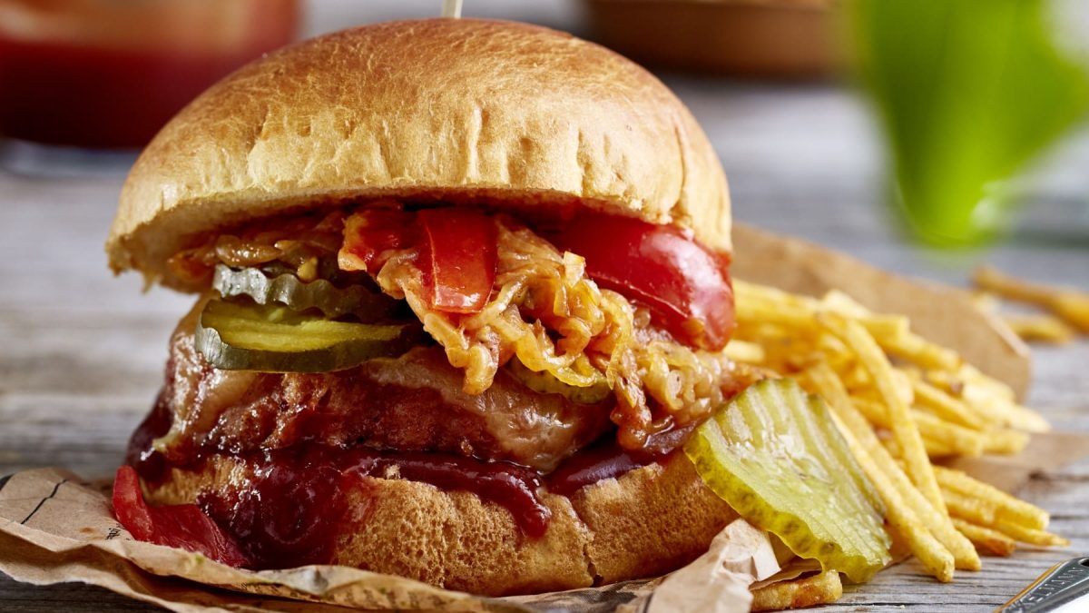 Camping-Burger auf Backpapier mit Kartoffel-Sticks im Hintergrund.