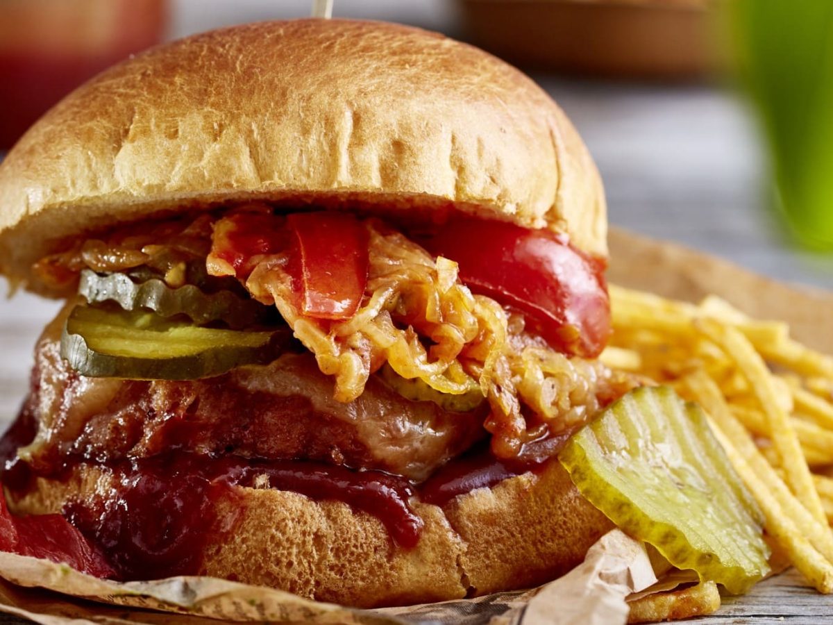 Camping-Burger auf Backpapier mit Kartoffel-Sticks im Hintergrund.