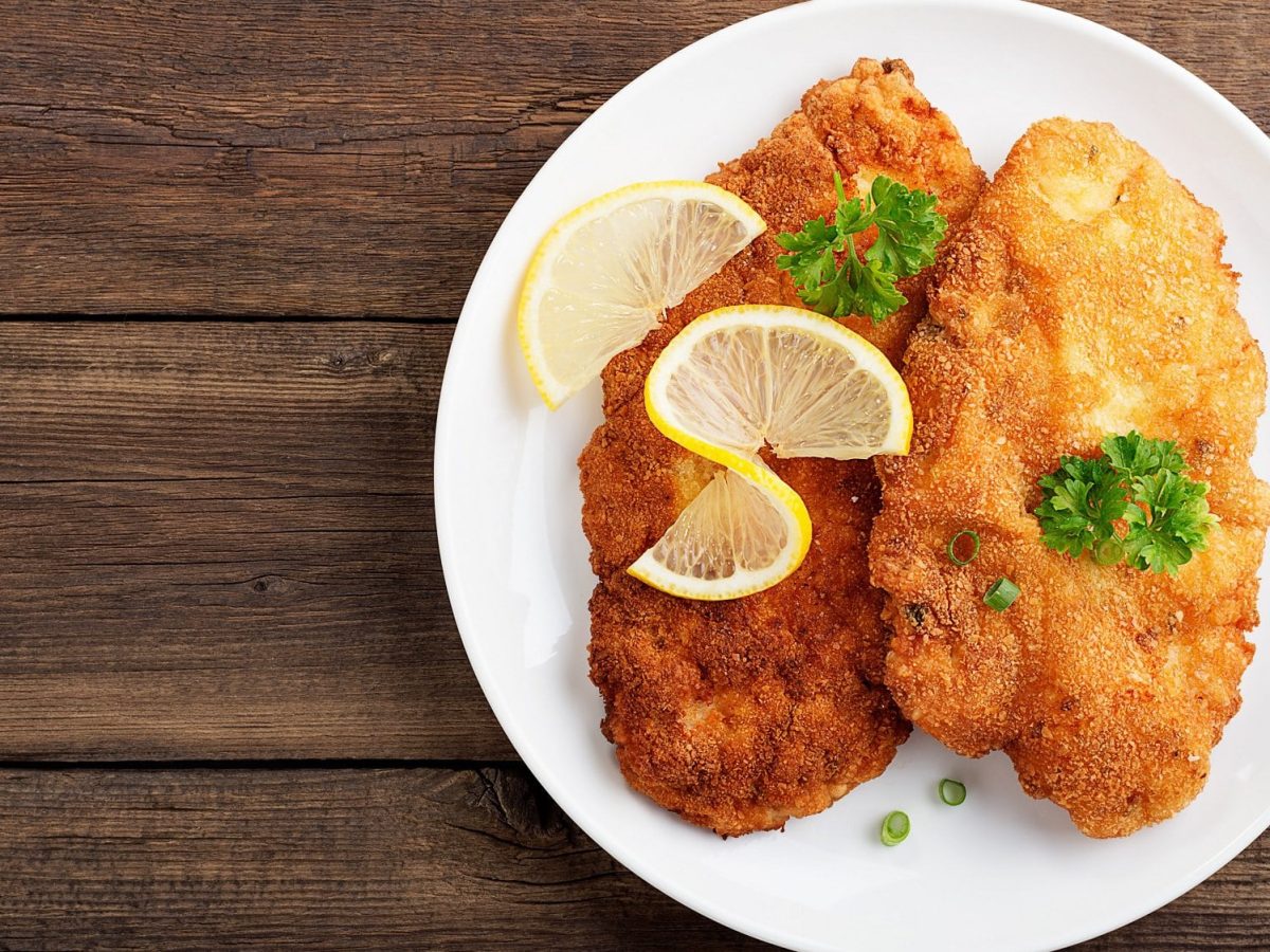 Draufsicht: Ein Teller mit zwei Brezen-Schnitzeln steht auf einem Holztisch.