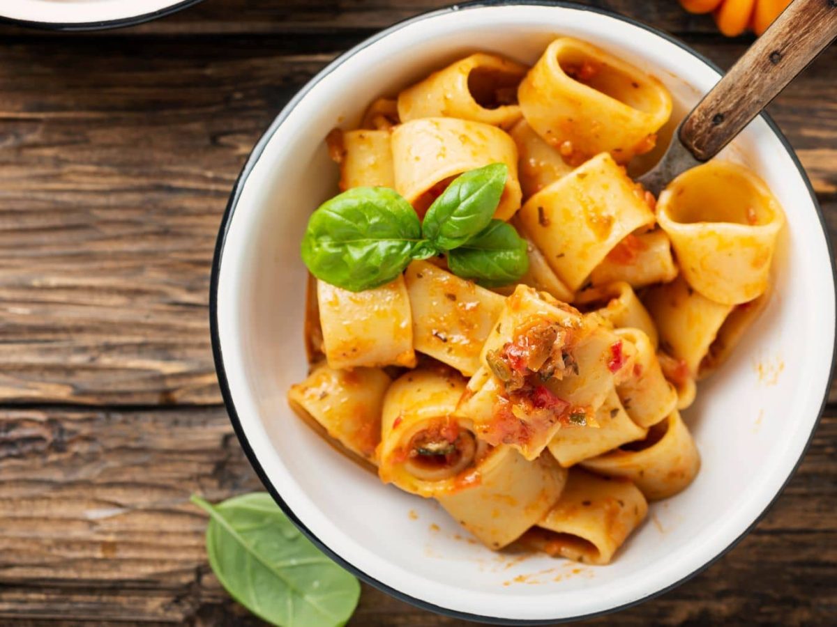 Pasta Calamarata alle Salsicce in weißem Teller mit Basilikum auf Holz. Draufsicht.