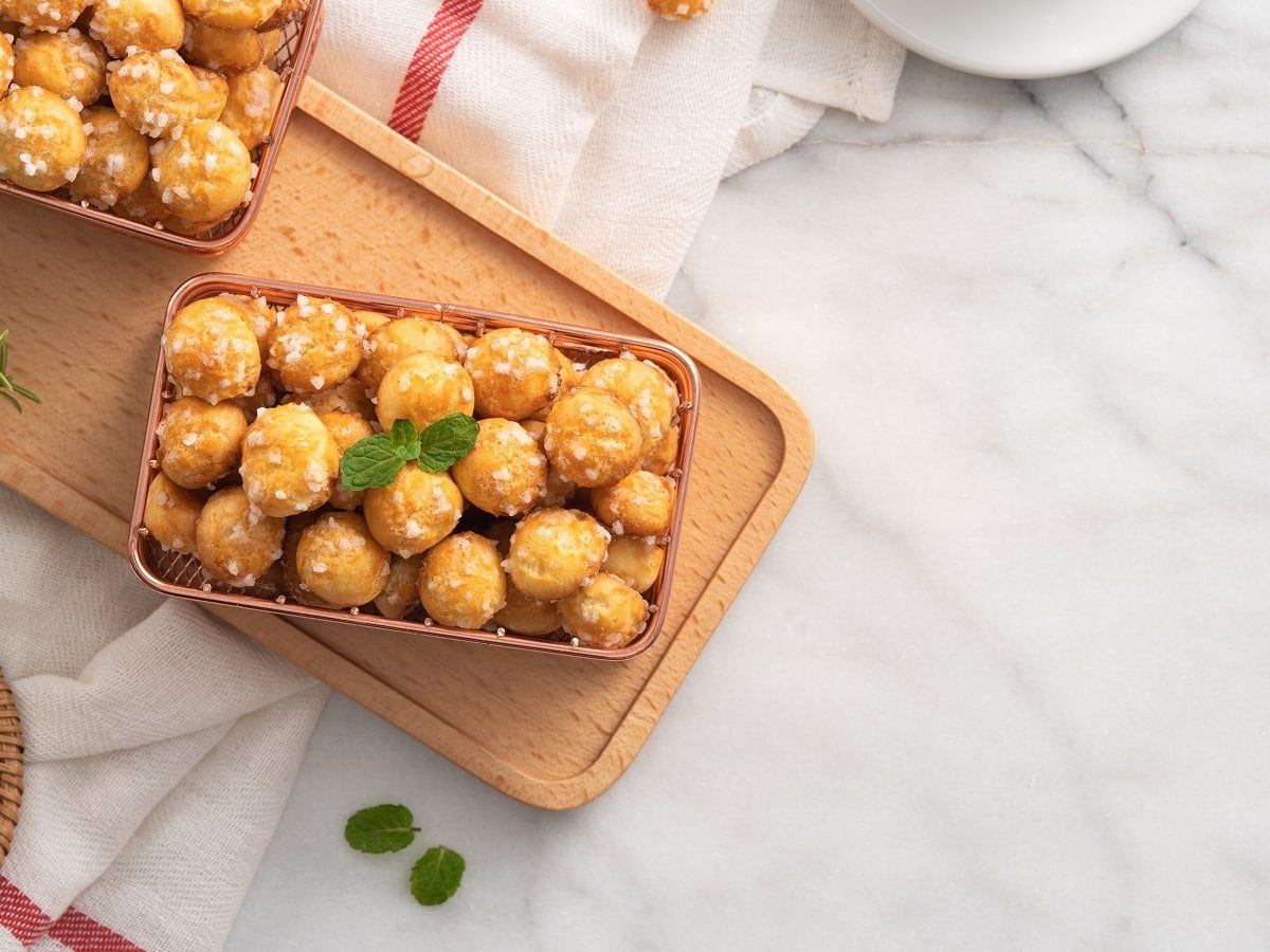 Ein Holzbrett mit Chouquettes auf einem hellen Tisch.