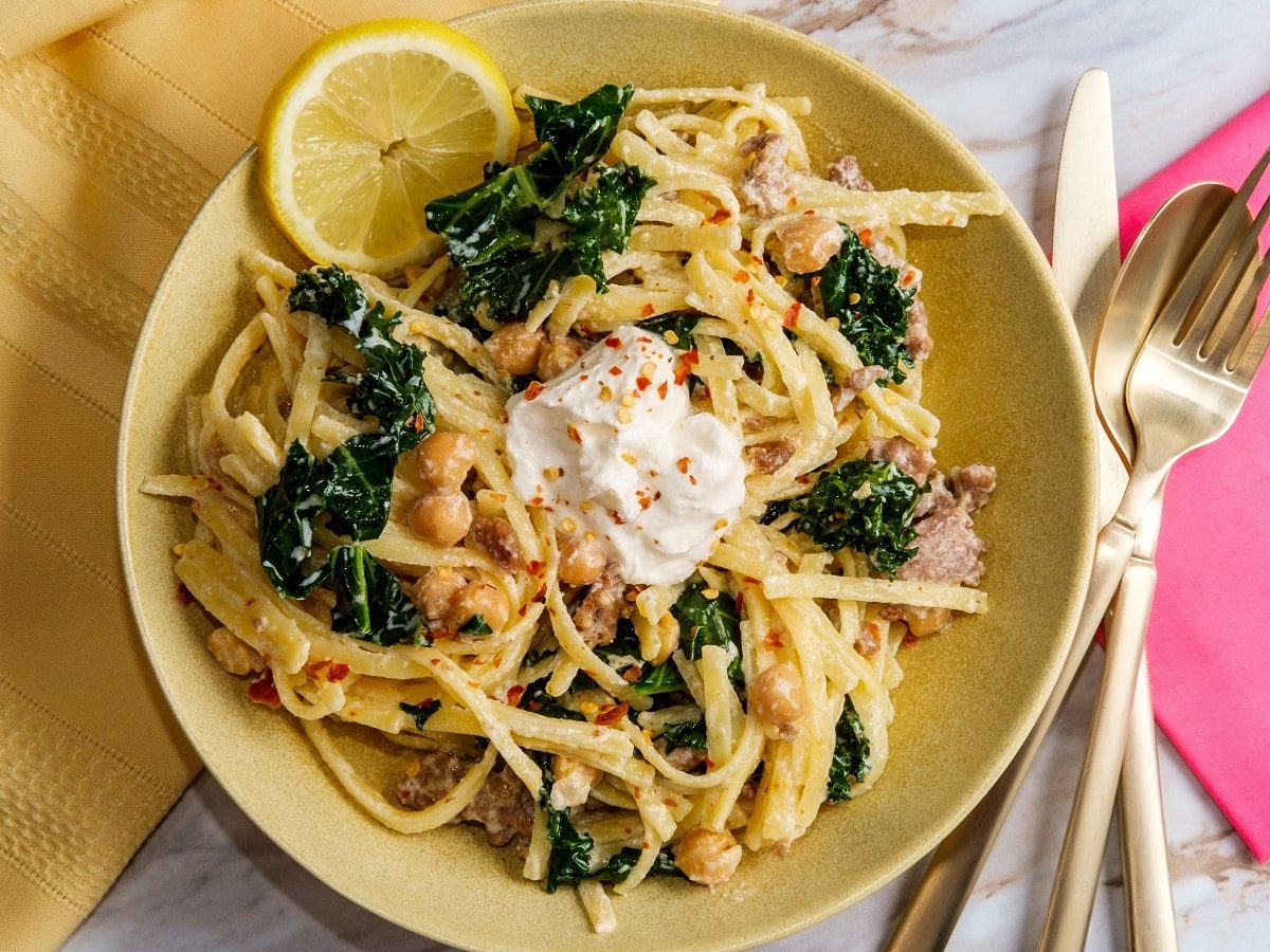 Ein gelber Teller mit Kichererbsen-Pasta mit Salsiccia und Ricotta auf einem weißen Tisch.