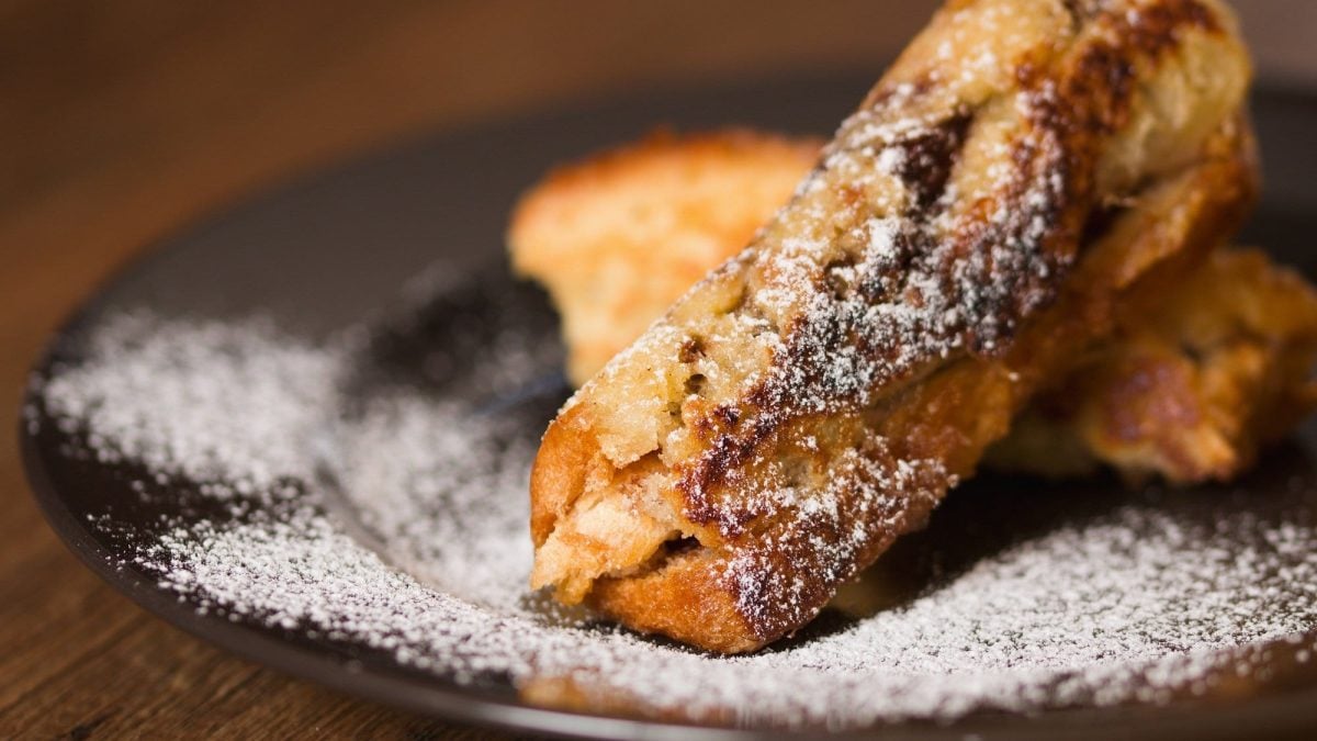 French-Toast-Röllchen mit Puderzucker bestreut auf einem Teller.