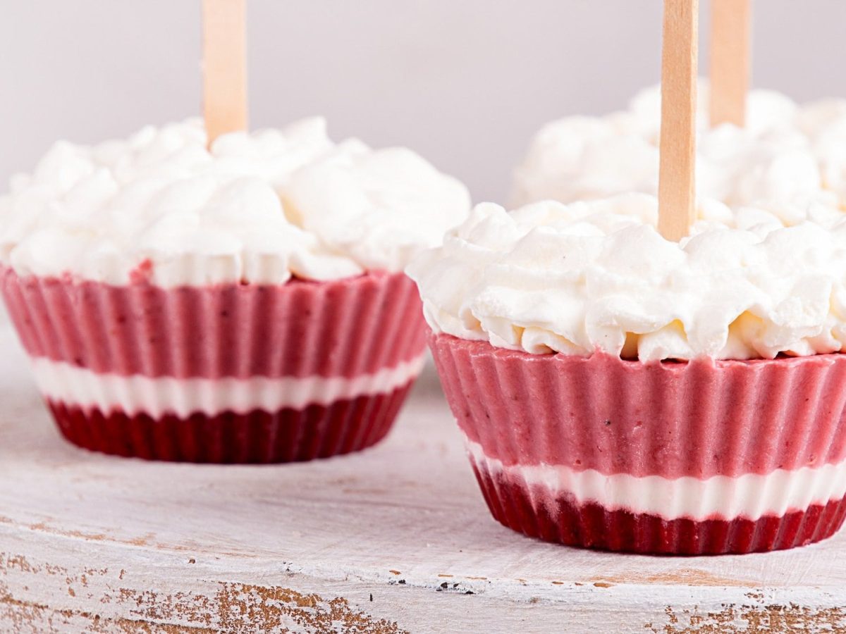 3 Frozen-Yogurt-Muffins mit Schlagsahne auf einem runden Brett.