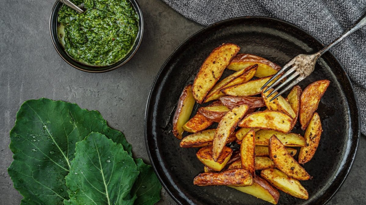 Ein Teller gebackene Kohlrabi-Wegdes mit einer Gabel, daneben eine Schale mit Pesto, alles Draufsicht.