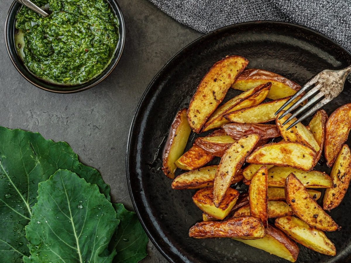 Ein Teller gebackene Kohlrabi-Wegdes mit einer Gabel, daneben eine Schale mit Pesto, alles Draufsicht.