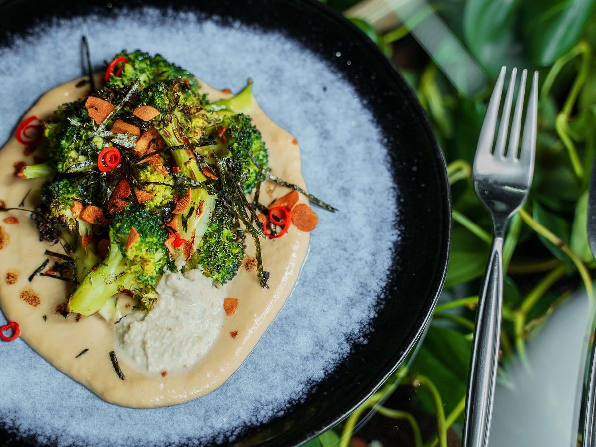 Ein hellblauer Teller mit geröstetem Brokkoli auf Miso-Hummus.