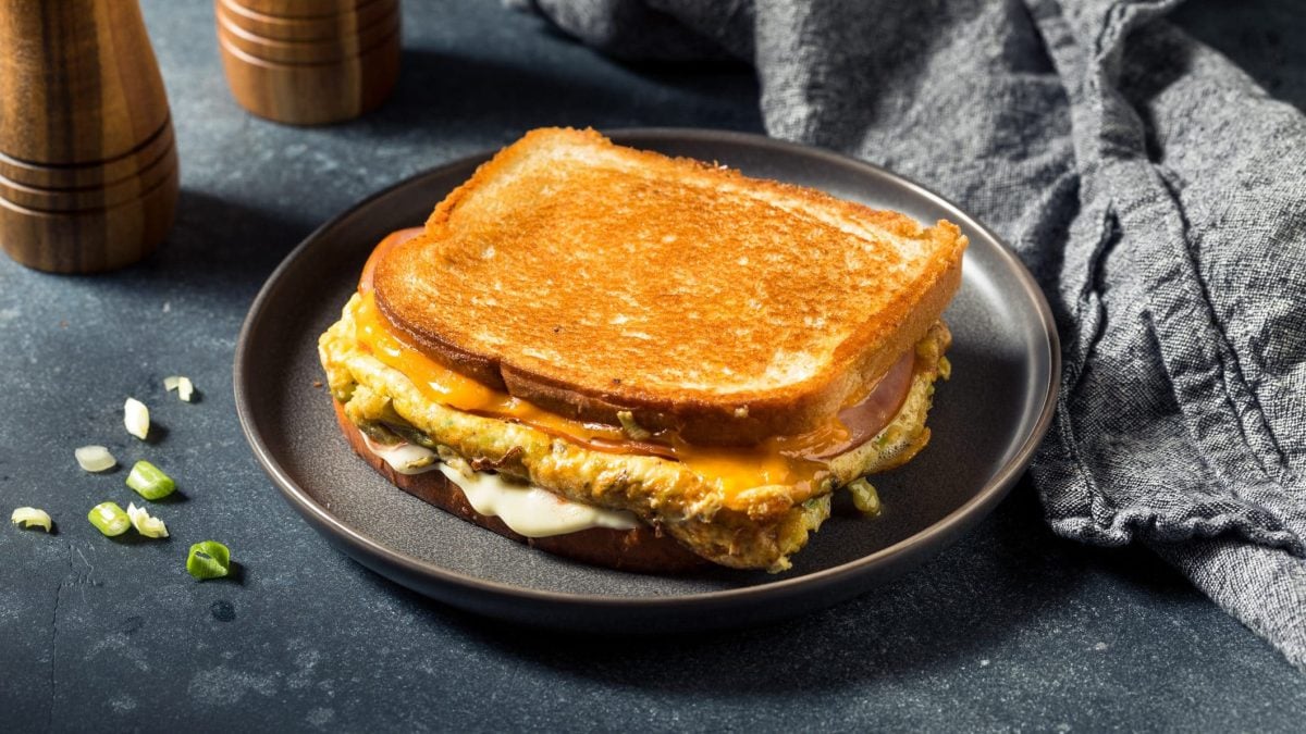 Ein Egg Drop Sandwich auf einem grauen Teller und dunklem Untergrund. Rehcts dahinter eine graue Serviette und links dahinter Salz- und Pfeffermühle.