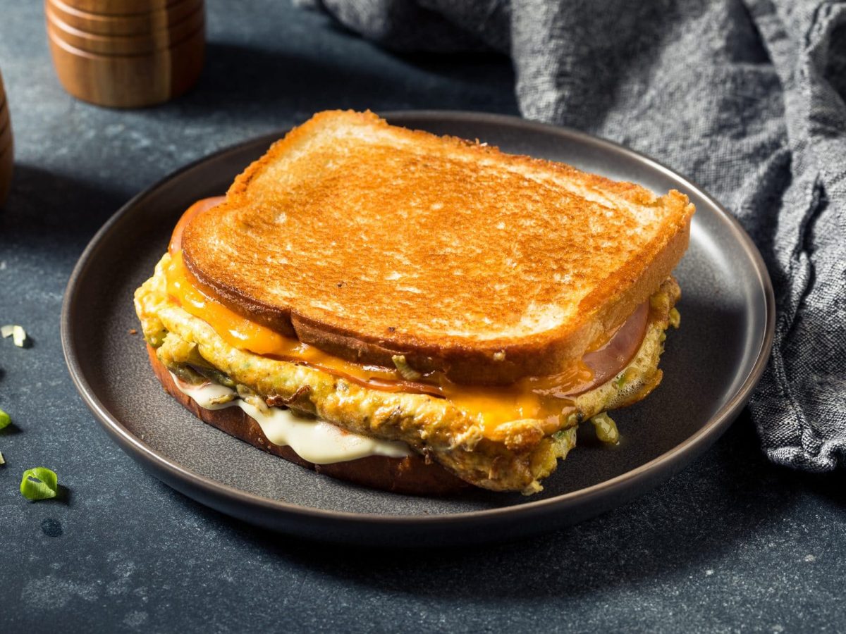 Ein Egg Drop Sandwich auf einem grauen Teller und dunklem Untergrund. Rehcts dahinter eine graue Serviette und links dahinter Salz- und Pfeffermühle.