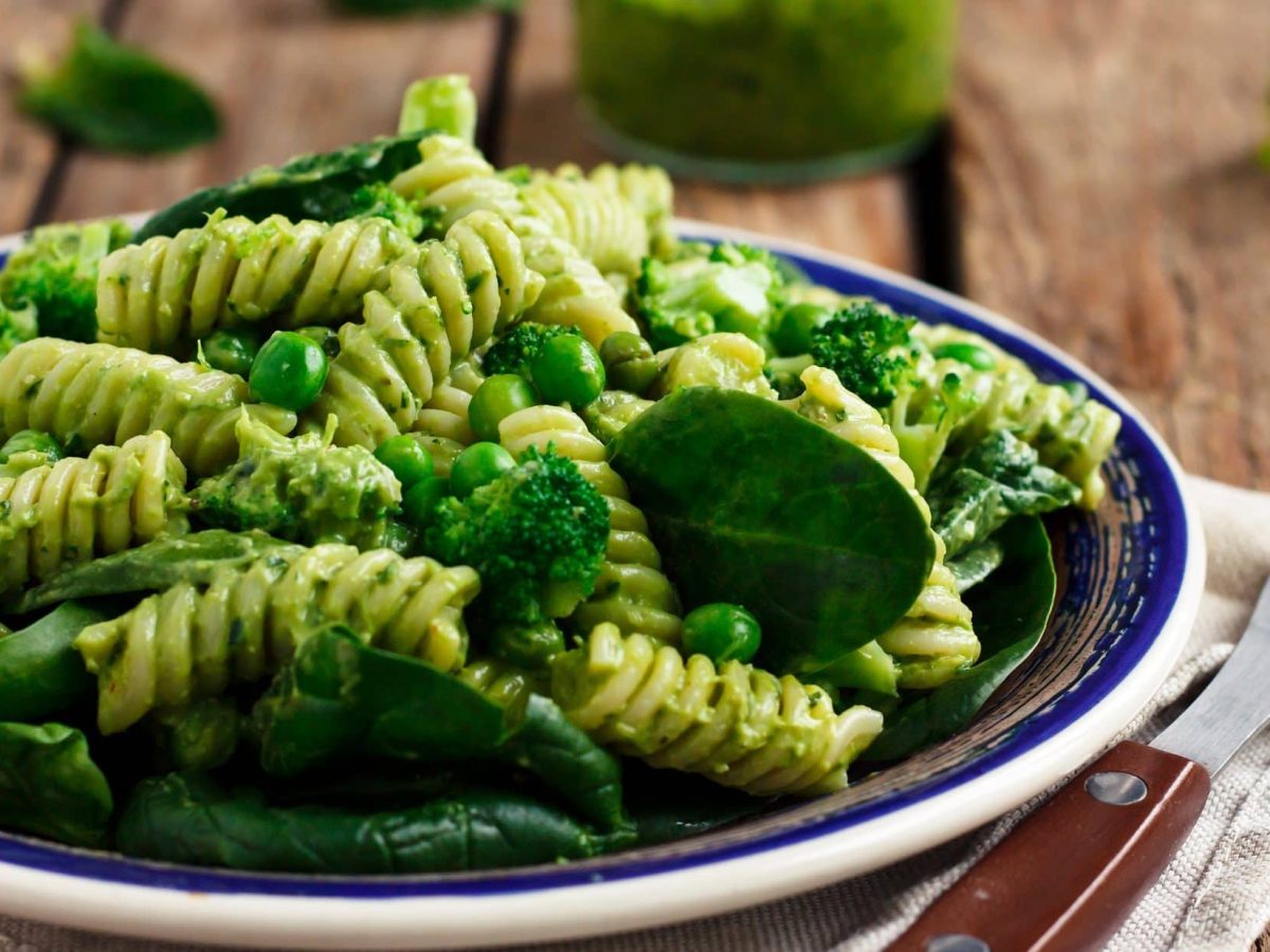 Ein Teller Green Goddess Nudelsalat mit Erbsen und Babyspinat, daneben eine Gabel.