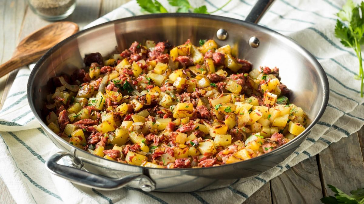 Eine Metallpfanne mit dem Kartoffelsalat auf einem weiß-blauem Tuch mit Petersilienzweigen, Salz- und Pfefferstreuer.