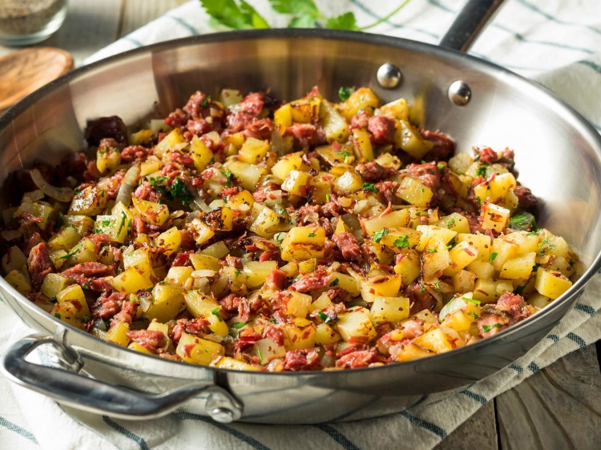 Eine Metallpfanne mit dem Kartoffelsalat auf einem weiß-blauem Tuch mit Petersilienzweigen, Salz- und Pfefferstreuer.