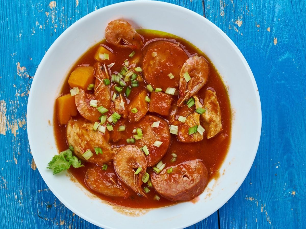 Ein weißer Suppenteller mit der Louisana-Soup auf einem blauen Holztisch.