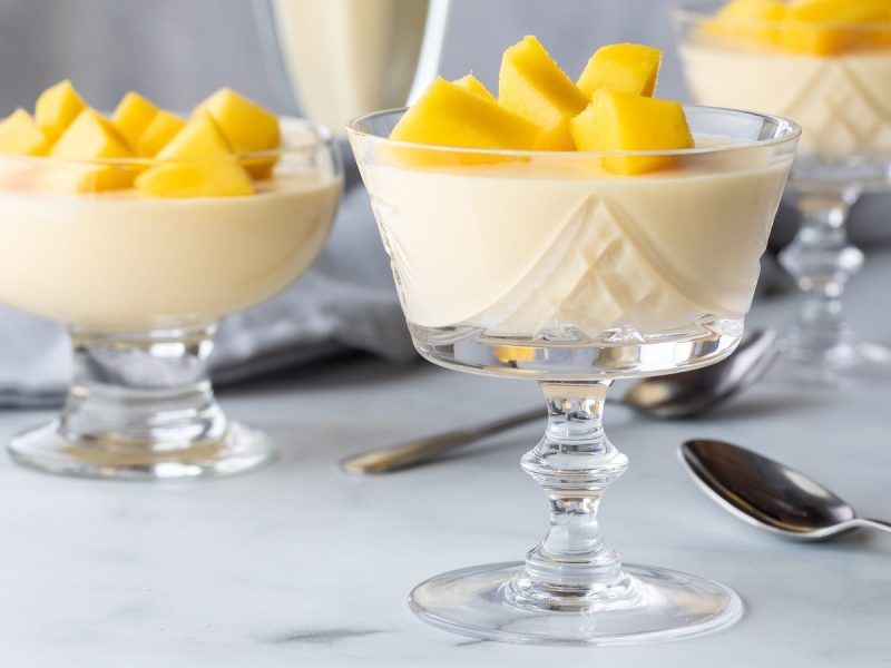 Drei Gläser mit Mango Mousse auf einem hellen Tisch.