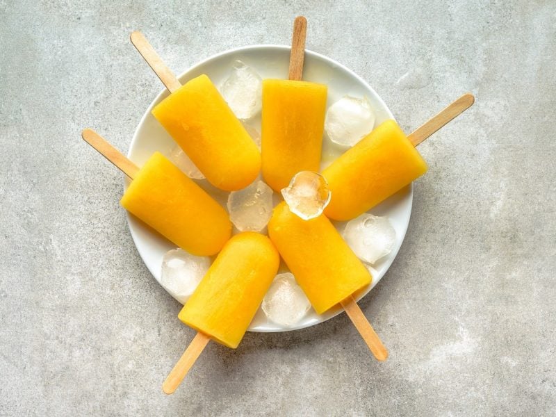 Ein Teller mit Mango Popsicles auf einem Steinuntergrund.