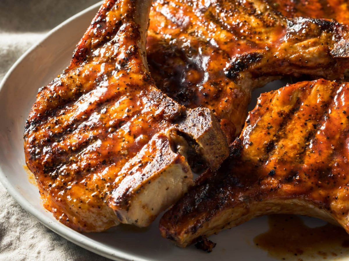 Marinierte Schweinekoteletts vom Grill auf weißem Teller und hellem Untergrund. Draufsicht.