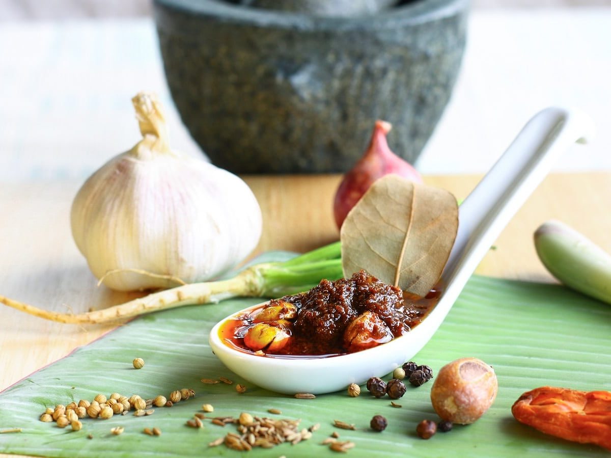 Ein Löffel mit Massaman Currypaste neben Gewürzen auf einem Bananenblatt.