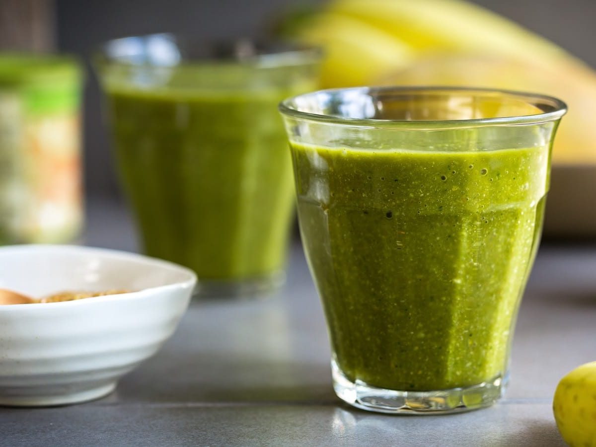 Ein Glas mit Matcha Mango Smoothie auf einem grauen Tisch