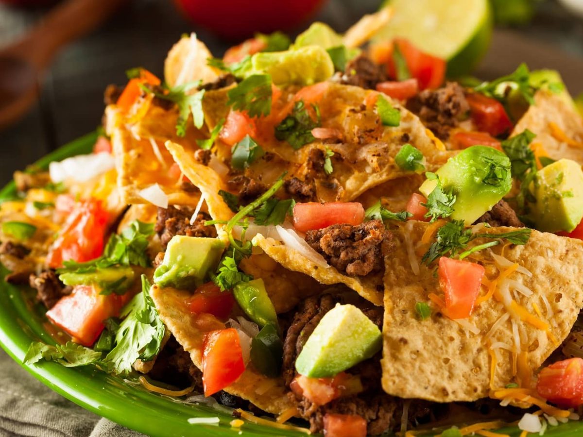 Ein grüner Teller mit dem Nacho-Salat auf einem Holztisch.