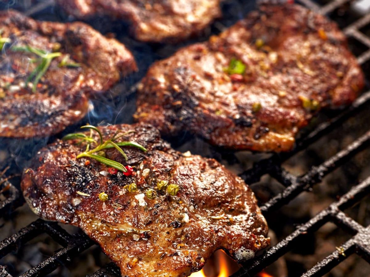 Gegrillte Nackensteaks mit Paprikamarinade auf Grillrost. Draufsicht.