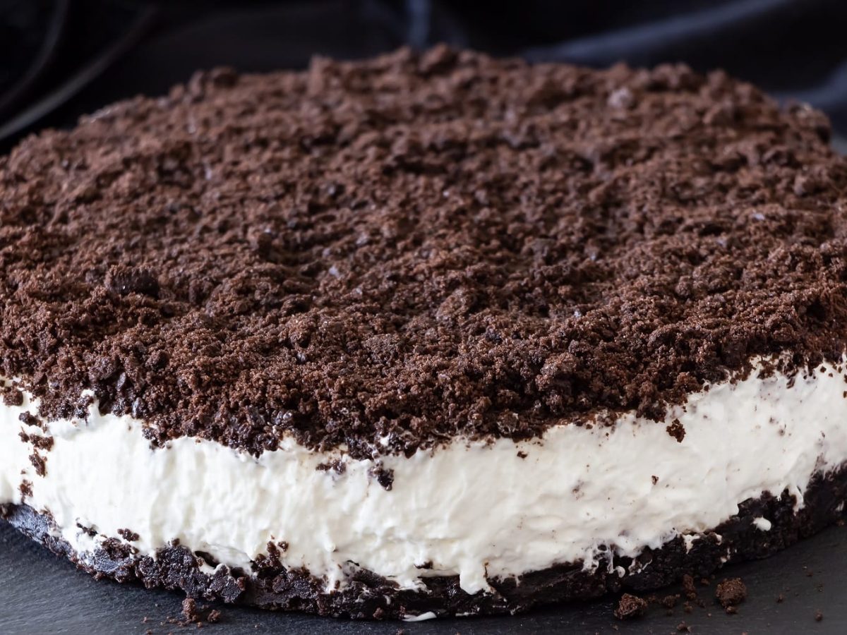 Die Oreo-Torte auf einer schwarzen Schieferplatte und im Hintergrund blauer Stoff.