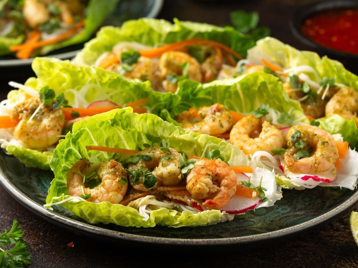 Ein dunkler Teller mit den Salat-Wraps gefüllt mit Garnelen und Reisnudeln.