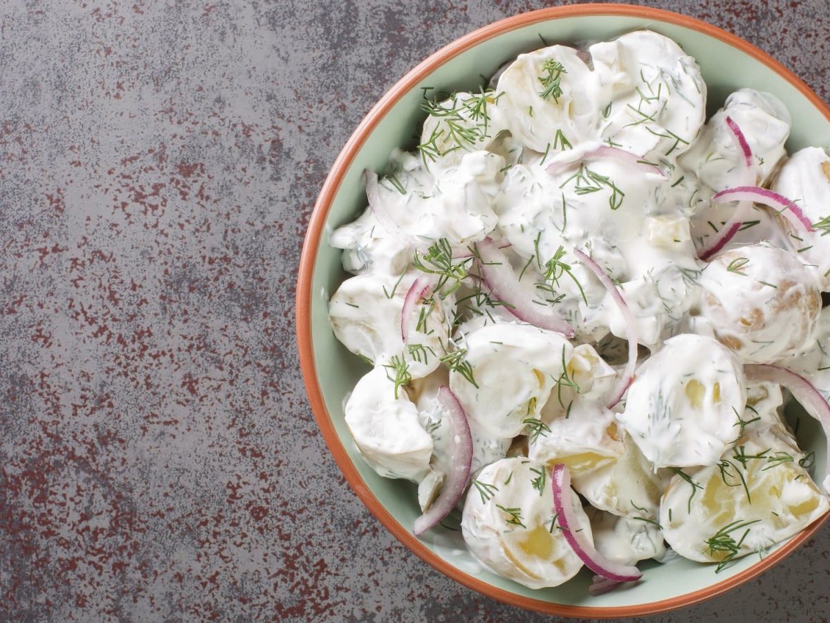 Eine Schüssel schwedischer Kartoffelsalat mit roten Zwiebeln, Dill und weißer Sauce.