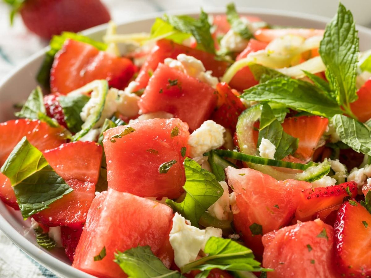 Eine weiße Schüssel mit dem Sommersalat auf einem blau-weiß-gestreiftem Tuch.