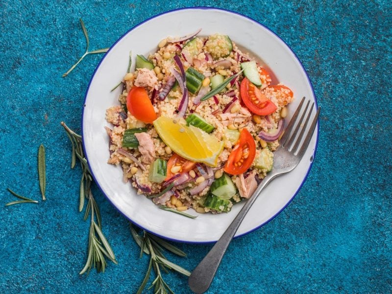 Draufsicht: auf einem blauen Untergrund steht ein weißer Teller mit einem Thunfischsalat mit Couscous.