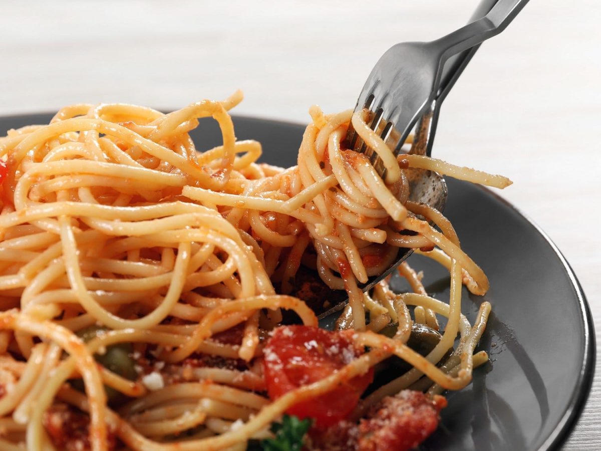 Ein Teller Tomaten-Creme-Pasta, eine Gabel und ein Löffel drehen gerade Spaghetti auf.