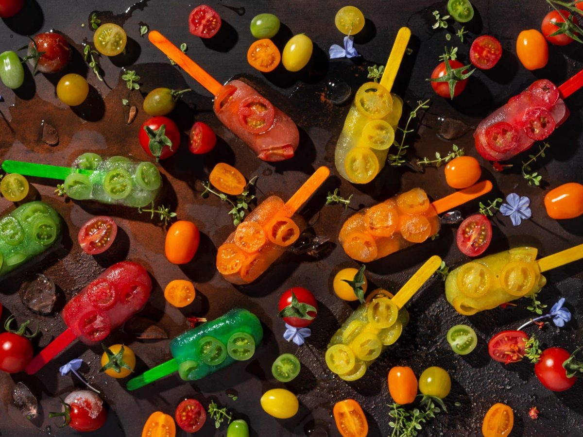 Kann man Tomaten einfrieren? Bunte gefrorene Tomaten und Tomaten in Wasser eingefroren am Stiel. Draufsicht.