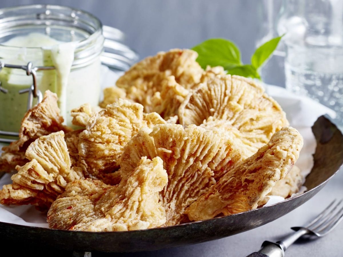 Vegane Calamari mit Tofu-Basilikum-Aioli auf einem dunklen Teller, grauer Hintergrund.