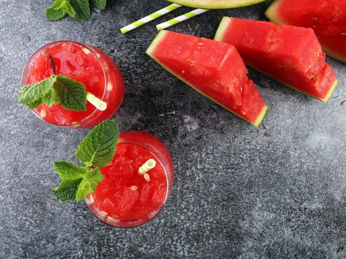 Zwei Gläser mit Wassermelonen-Minze-Smoothie auf einem grauen Tisch.