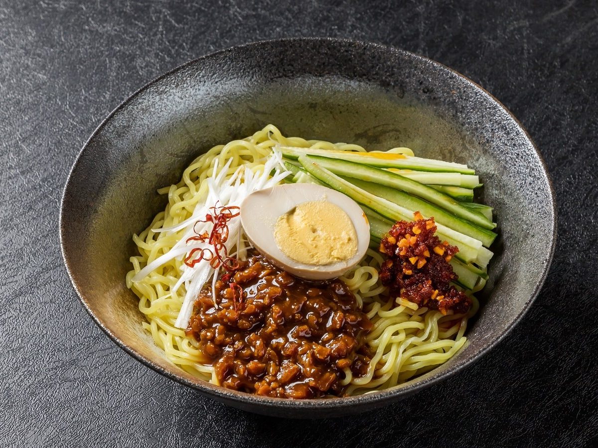 Eine Schüssel mit Zha Jiang Mian auf einem dunklen Tisch.