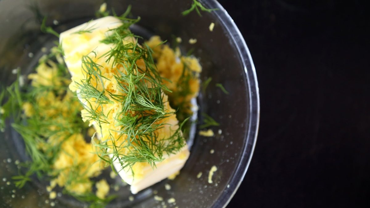 Eine Glasschüssel mit Zitronen-Dill-Butter auf einem dunklen Tisch.